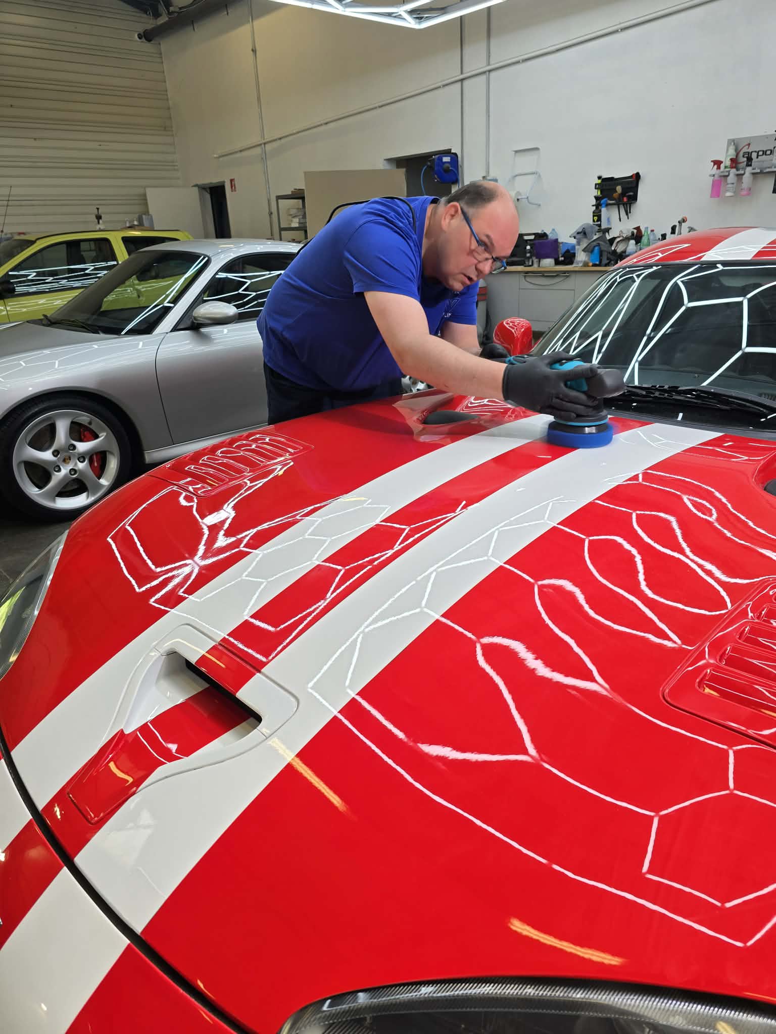 Polissage du capot d'une Dodge Viper : les reflets de la rampe de détaillage se lisent nettement sur le vernis